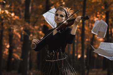Obraz premium Young woman plays violin over the music notes flying away and fall park background