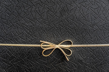 Gold double holiday bow on black textured background, placement