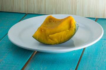 Boiled pumpkin pieces on a white plate and wooden background
