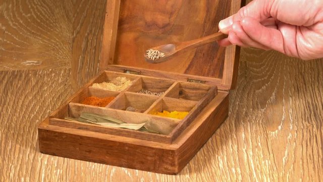 Collection of different oriental indian curry spices in wooden box with cumin in wood spoon in senior man hand