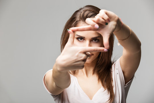 Closeup of young beautiful brunette woman making frame with her fingers, over gray background