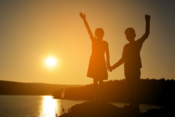 Silhouette of childrend open hand on the rock in river at the sky sunset