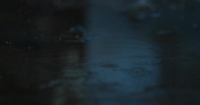 Raindrops falling into the ground. Water drops falls on the black surface. Macro shot, close up, Slow Motion