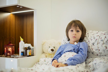 Naklejka premium Cute sick child, boy, staying in bed, playing with teddy bear