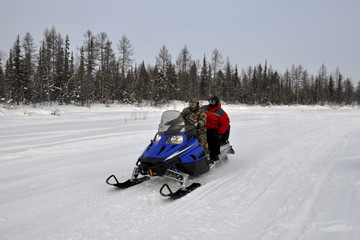 Two men ride on a snowmobile on the frost river in the winter forest