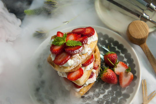 Delicious dessert: waffles with fresh strawberries and cream close-up on a plate. horizontal, Image Blurred from vapor or Dry ice for Decorate. 