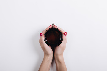 Top view of a woman's hands with red manicure holding a cup of t