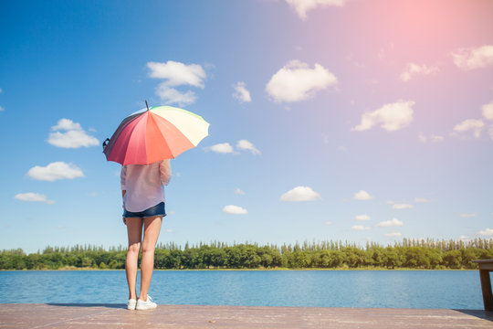 young woman standing with holding  colorful umbrella beside river