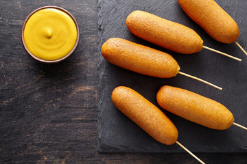 Corn dog traditional American street food deep fried hotdog meat sausage snack treat on stick unhealthy eating on dark wooden background table
