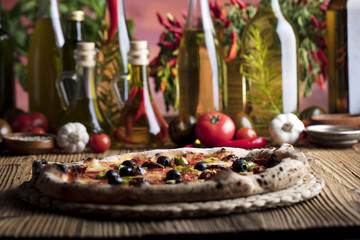 Delicious, tasty and fresh, rustic Italian pizza, served on wooden table. Bunch of tomatoes, chili, basil, garlic in background. Bowls with different kinds of pepper. Many bottles of olive oil