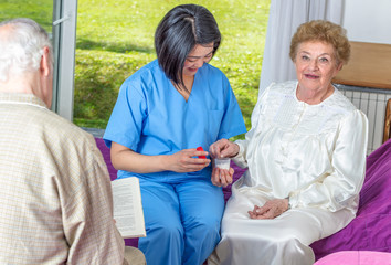 Asian nurse giving pills to elderly patients in hospital