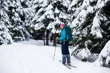 Girl in bright clothes with a backpack is traveling on ski tours