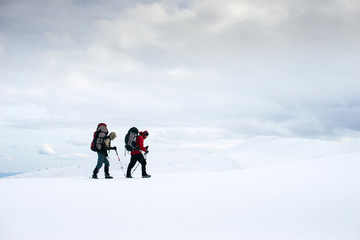 Fototapeta na wymiar Two friends with backpacks are tracking in the snowy and windy