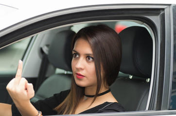 Fototapeta na wymiar Closeup young woman sitting in car giving the finger angrily, as seen from outside drivers window, female driver concept