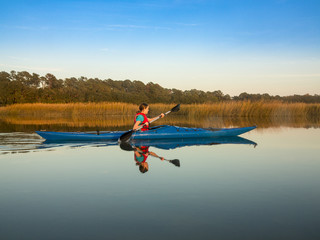 Fototapeta na wymiar Teen kayaking through glassy water