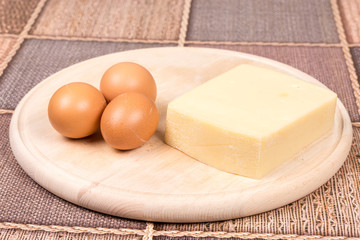 Raw eggs and yellow pizza cheese on the cutting board