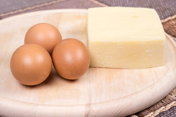 Raw eggs and yellow pizza cheese on the cutting board