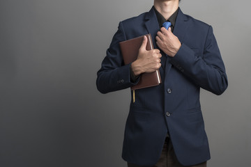 Obraz na płótnie Canvas Close up of businessman in blue suit holding books on gray backg