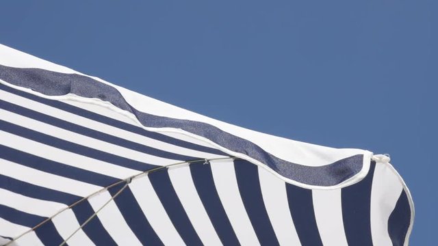 Umbrella fabric made for protection from the sun slow motion 1080p FullHD footage - Beach striped blue parasol against clear sky moving on wind slow-mo 1920X1080 HD video