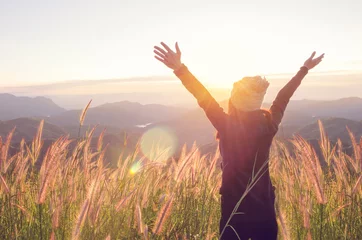 Muurstickers Carefree Happy Woman Enjoying Nature on grass meadow on top of mountain cliff with sunrise. Beauty Girl Outdoor. Freedom concept. Len flare effect. Sunbeams. Enjoyment. © oatawa