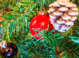 Red ornaments and pine cones on green artificial Christmas tree 