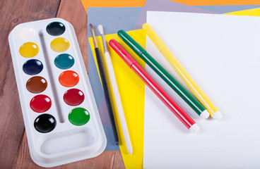 Naklejka premium Paper, watercolors, paint brush and markers on wooden table