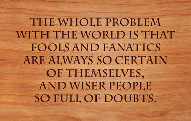 The whole problem with the world is that fools and fanatics are always so certain of themselves, and wiser people so full of doubts - quote on wooden red oak background