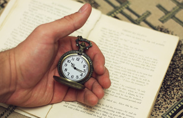 Old pocket watch in the hand on the background of the book