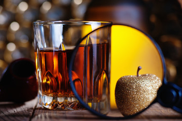 Glass of whiskey, magnifying glass, golden apple and smooking pipe 