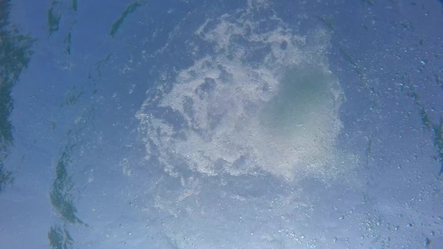 Man swims over a camera that's lying on the bottom of the sea. Clear blue water.