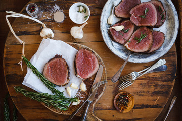Sliced rare tenderloin steak with garlic, rosemary over wooden table. Roasted Beef medium rare mignon meat.