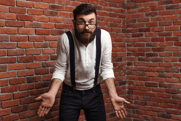 Young handsome man in glasses gesturing over brick background.