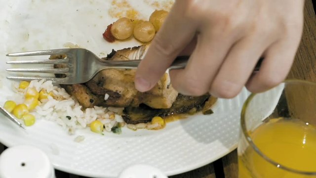 Close up of person's hands eating meat and fried rise with vegetables. Woman enjoying dinner in a restaurant. Healthy food on white plate.