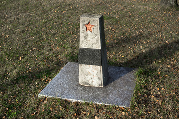 Memorial and grave of unknown soviet soldier from red army. Gravestone with red star. Grass and leaves around place