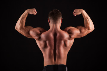Fototapeta na wymiar Rear view of healthy muscular young man with his arms stretched out isolated on black background
