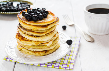 Stack of homemade pancakes with black currant, vintage white plate and fork, cup of coffee, wooden table.