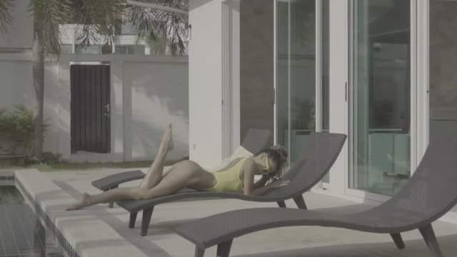 Beautiful healthy sexy woman with fit body in fashionable elegant yellow bikini swimsuit and sunglasses lying down on sunbed beside the swimming pool. Summer relax concept - video in slow motion