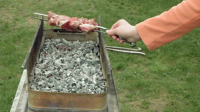 Girl puts barbecue bbq skewers with red meat on brazier with hot coals embers. Outdoors picnic concept.