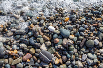 Wet bright shining different colored pebble stones and sea foam