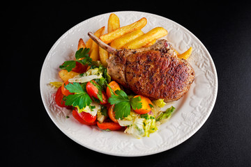 Grilled pork cutlet meat garnished with potato and salad on black table