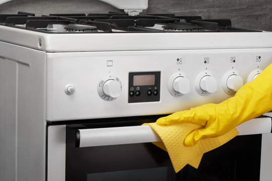 Hand in yellow rubber glove cleaning white stove with rag