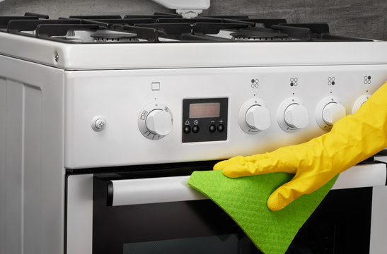Hand in yellow glove cleaning white stove with green rag