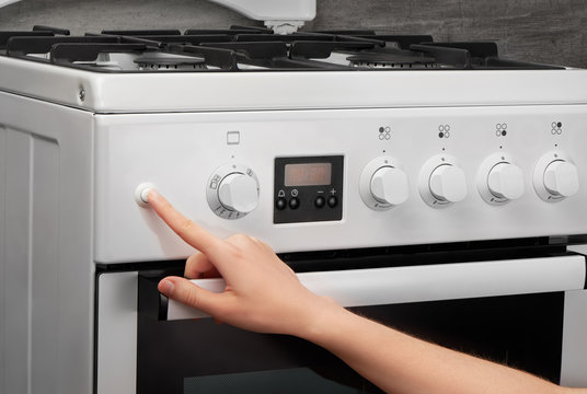 Female hand turning on white kitchen gas stove