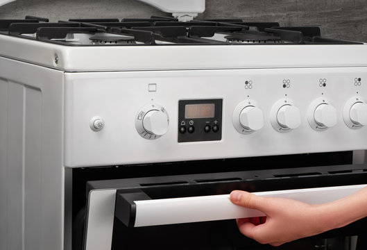 Female hand opening oven in white kitchen gas stove