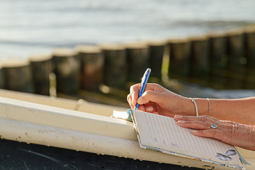 Frau macht Notizen am Strand in einem Tagebuch oder bullet journal