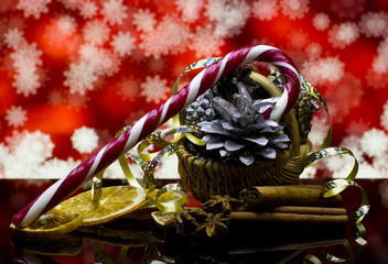 Christmas and New Year`s natural organic decorations with silver pine cones, dry orange fruits,cinnamon, star anise,candy cane on a black reflection surface and red bokeh background with snowflakes.