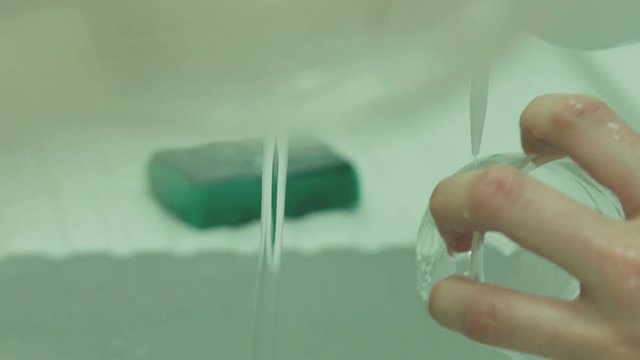 Slow motion: Close-up: washing the glass beaker. Chemical vessels. Laboratory chemical washes the dishes under running water. Equipment for chemical laboratory.
