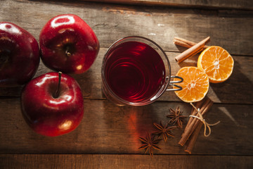 Mulled wine on wooden background with red apples, cinnamon sticks, anise seeds and cut oranges.
