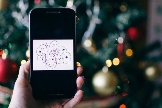 person takes a photo on a smartphone of HAPPY NEW YEAR with a christmas background