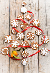 Christmas tree made from gingerbread cookies and red ribbon decorated with small oranges on a wooden background.  Holiday, celebration and cooking concept. New year and christmas postcard.